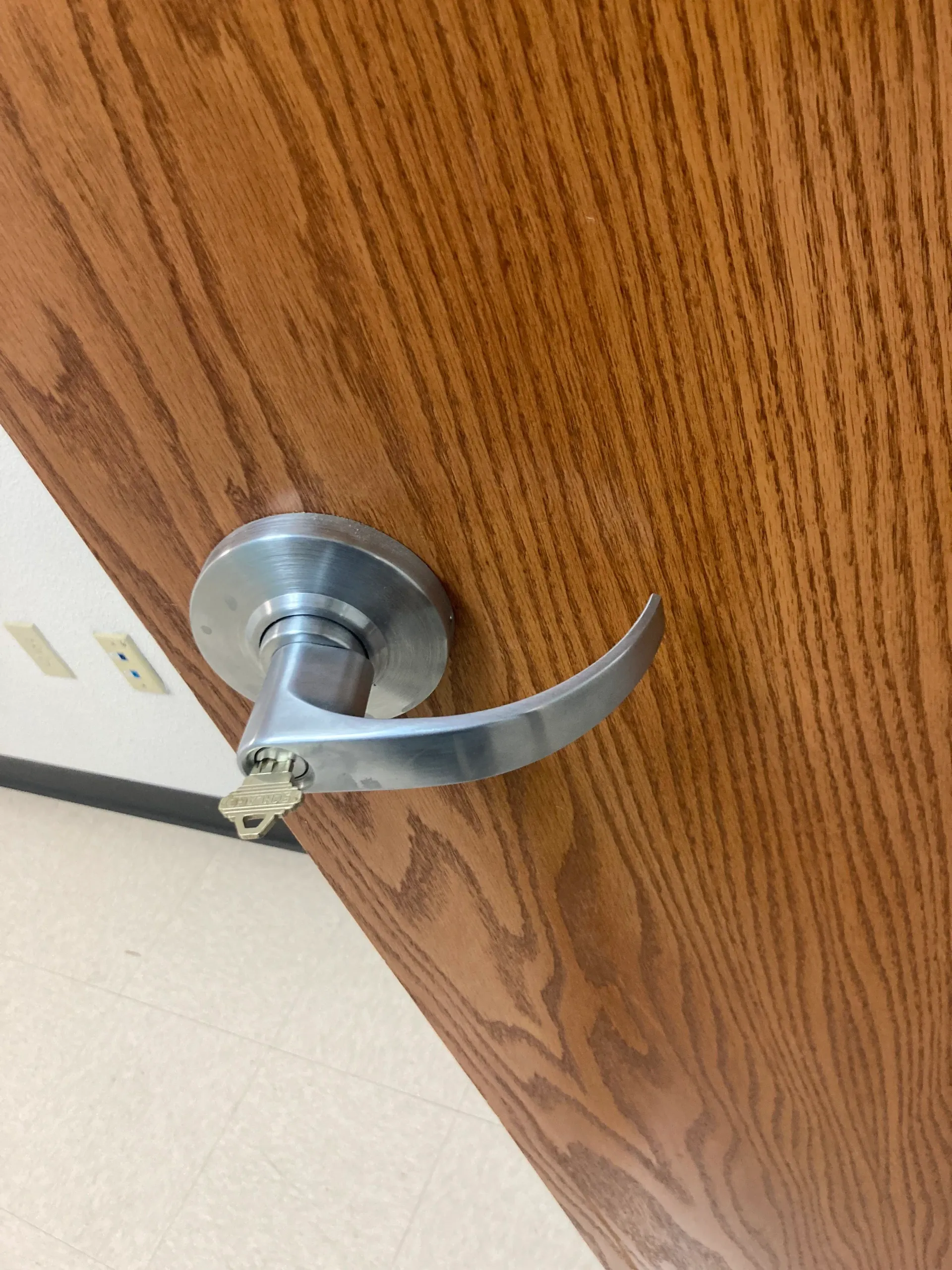 Close-up of a silver door handle on a wood-grain door, with a key inserted in the lock.