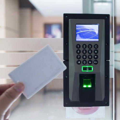 Hand holding a white card near a biometric access control keypad with green-lit scanner