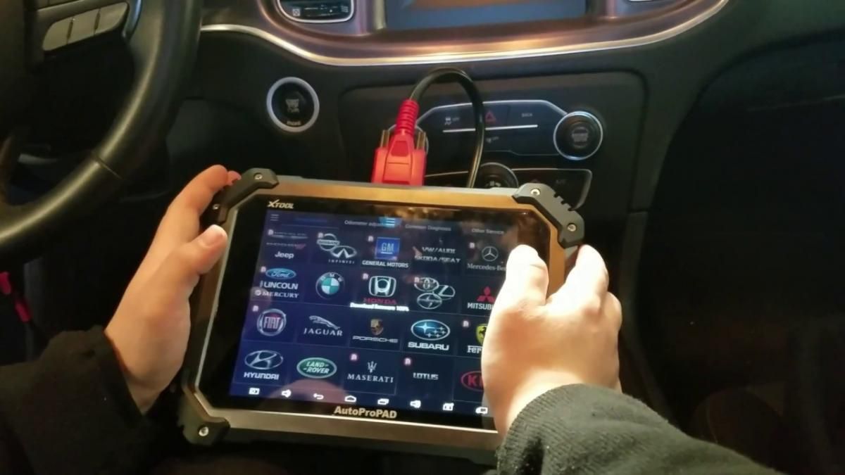 Hands holding a tablet with a car diagnostic app inside a vehicle dashboard.