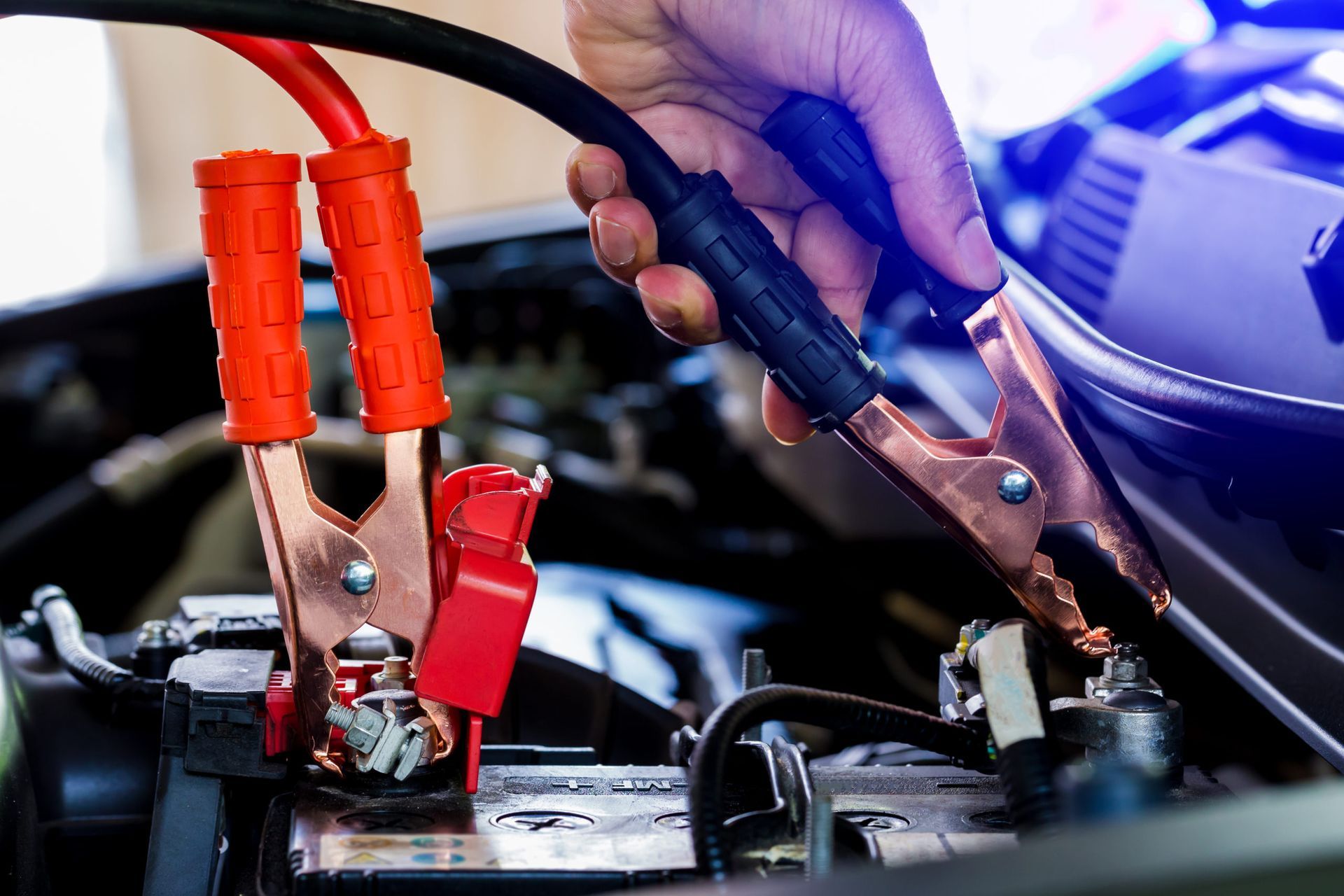 Hands connecting jumper cables to a car battery in an engine bay