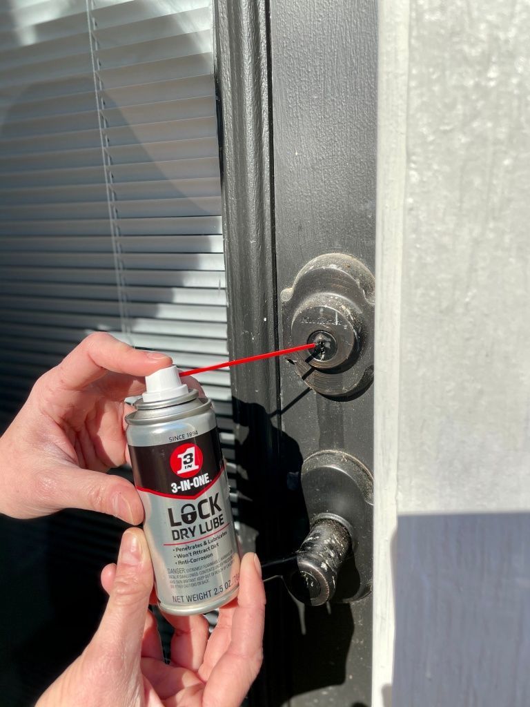 Hand spraying lock lubricant into a door lock on a black door handle