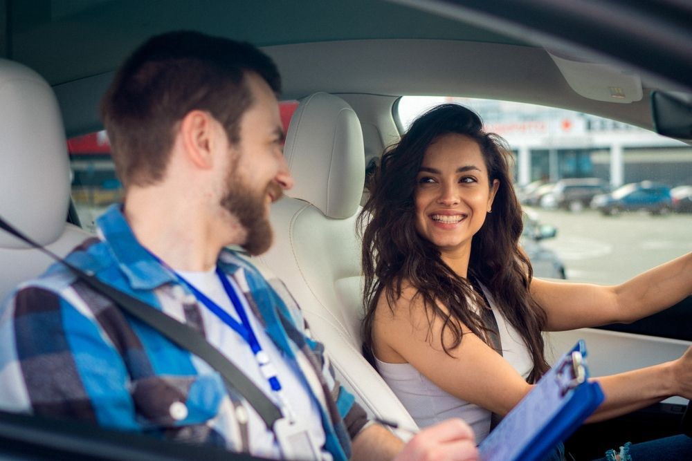 Two people smiling in a car, one driving and one holding a clipboard