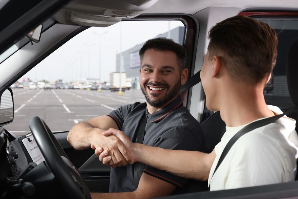 Two men shaking hands inside a vehicle, smiling at each other