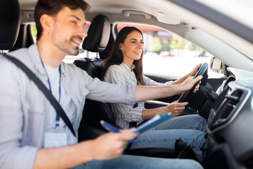 Two people in a car, one driving and one taking notes with a tablet.