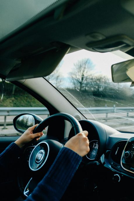 Driver’s hands on a steering wheel inside a car, with a snowy roadside visible through the window.