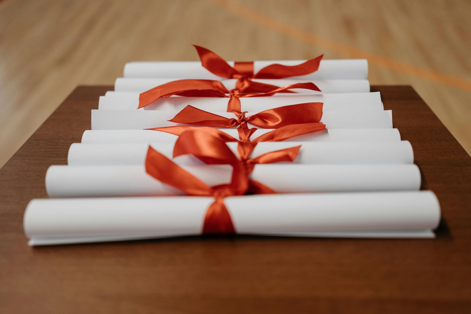 Rolled white papers tied with red ribbon on a wooden table, arranged in a row