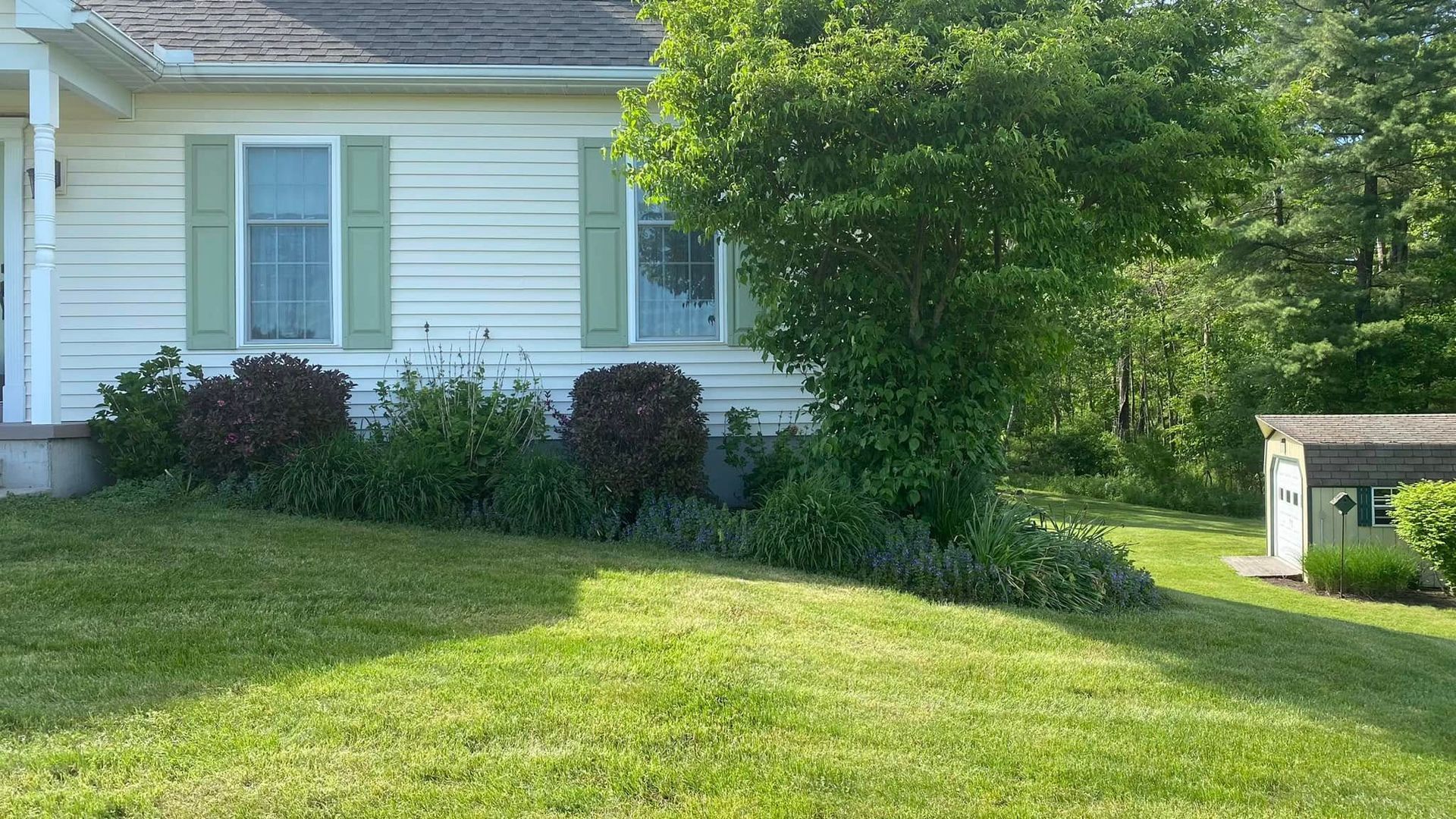 A white house with green shutters and a lush green lawn in front of it.