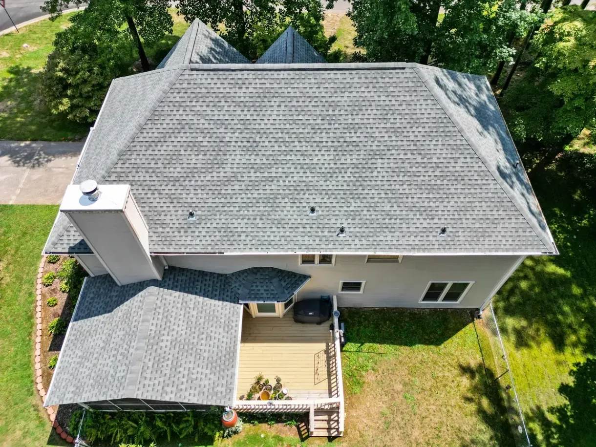 Overhead view of a house with a gray shingled roof, deck, and chimney in a grassy yard.