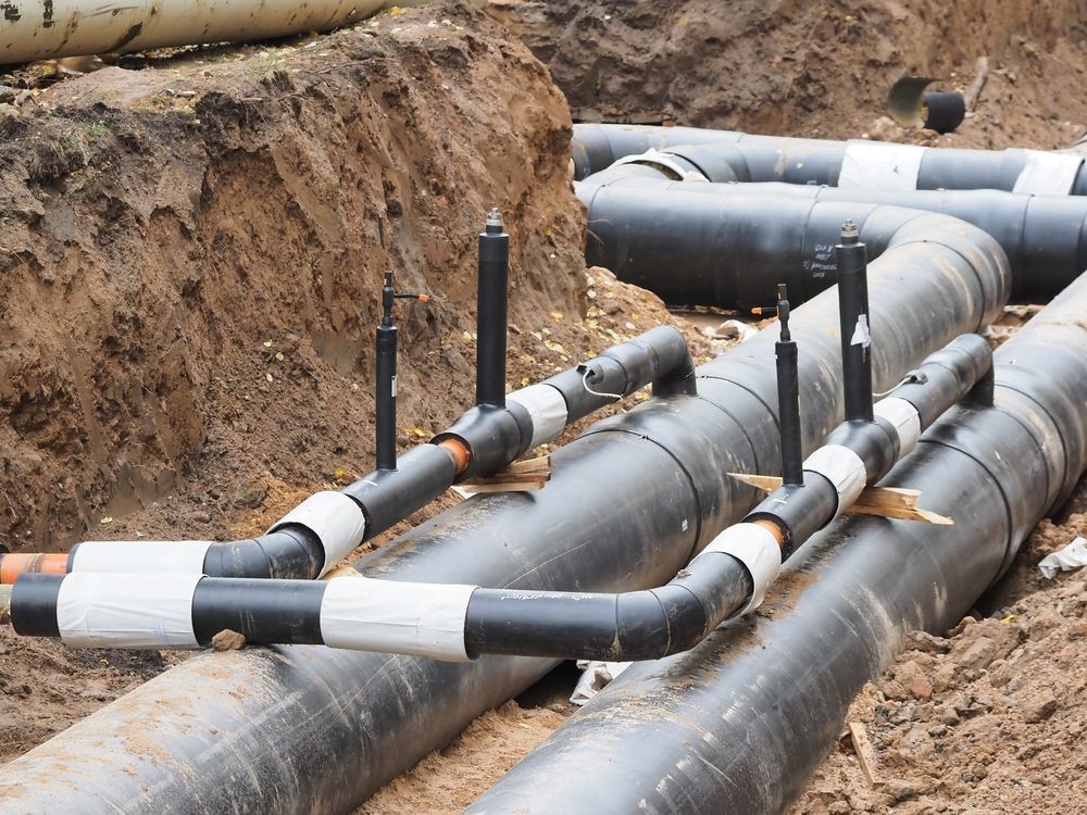 Black pipes with white tape and vertical black posts in a trench, likely for infrastructure.