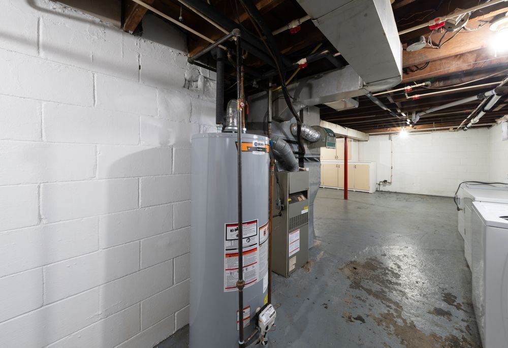 Basement interior with water heater, furnace, and exposed ceiling beams; gray and white.