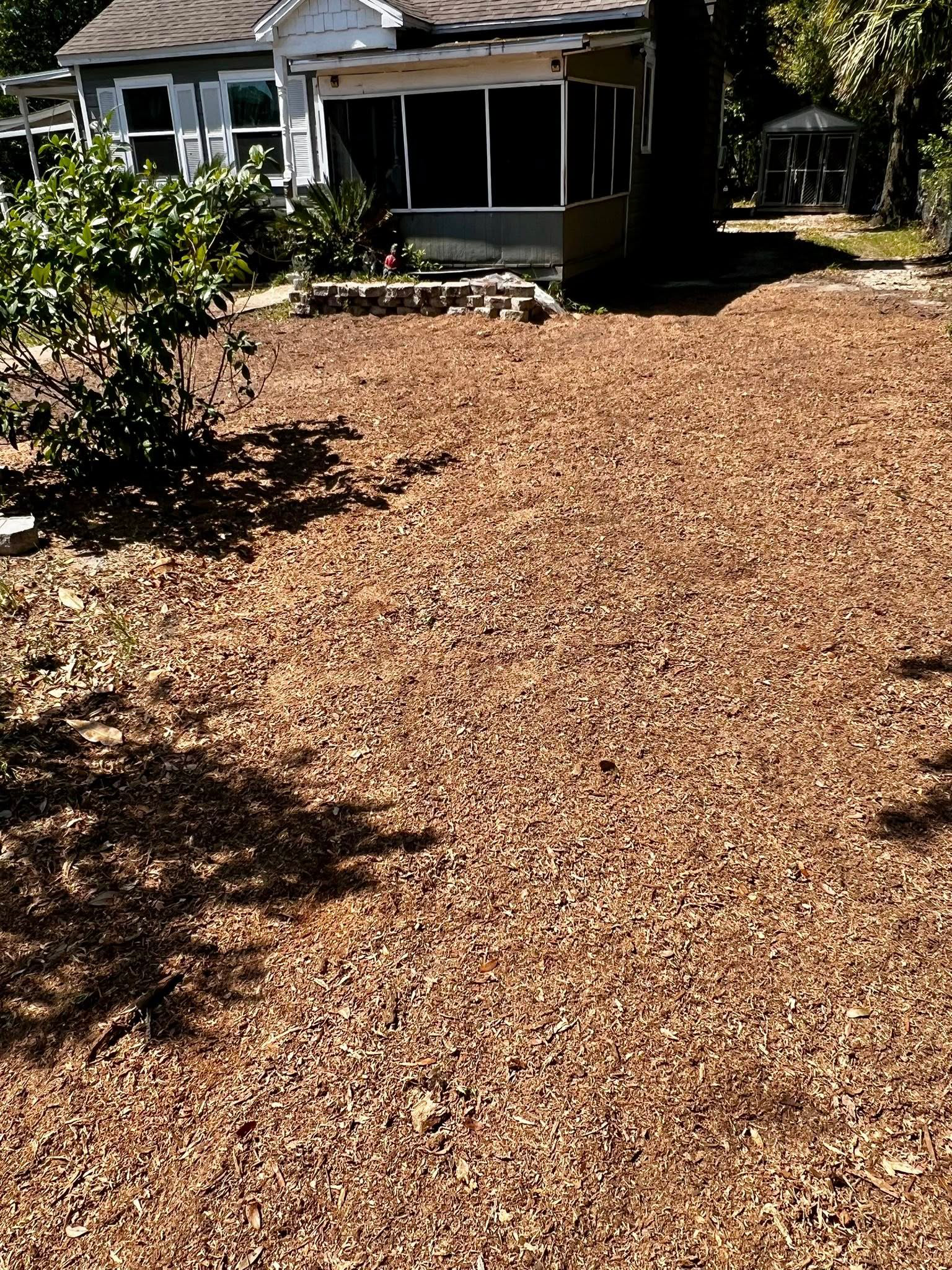 A gray house with a screened-in porch sits behind a large yard covered in brown fallen leaves.