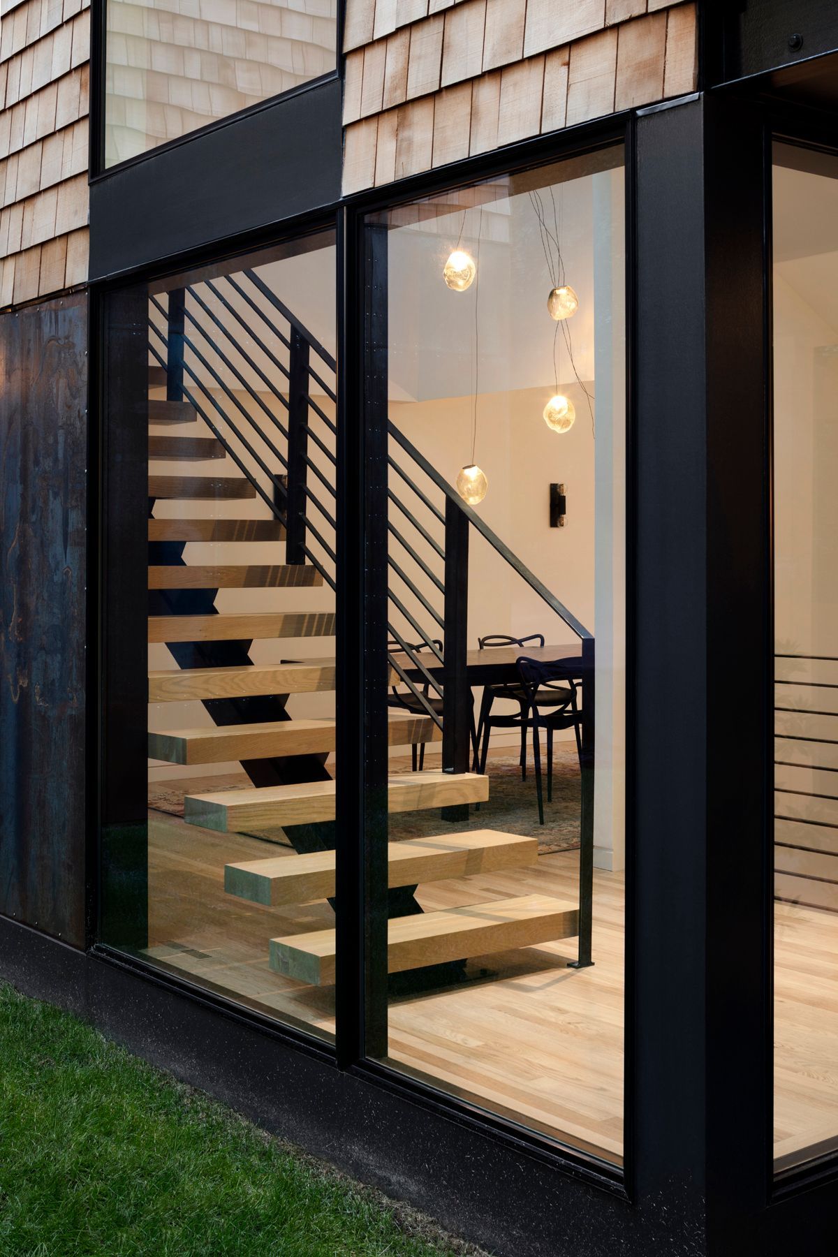 Modern glass-walled staircase inside a sleek house, with wood steps and warm interior lighting