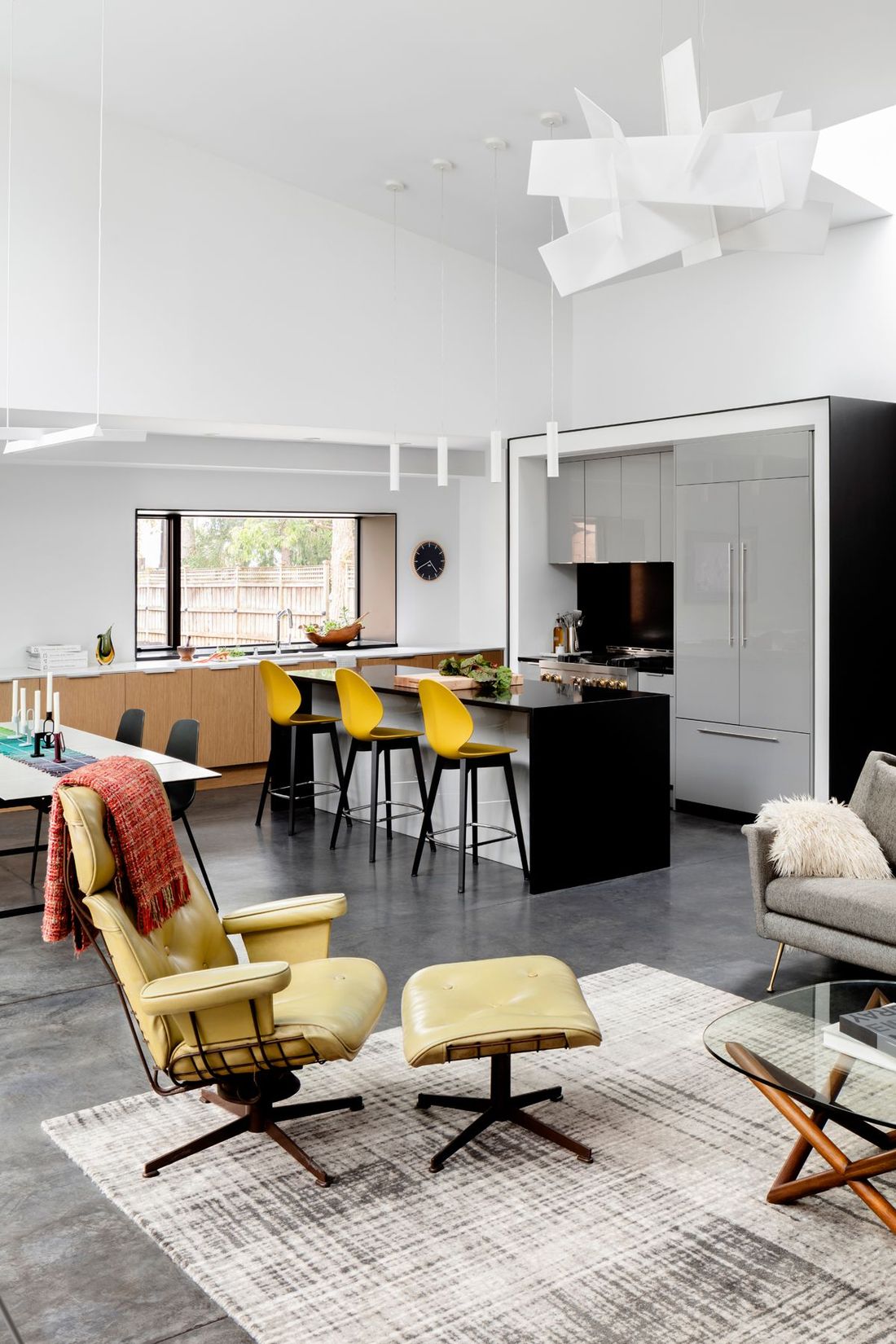 Modern open-plan living room with yellow chairs, gray sofa, kitchen island, and sculptural ceiling light