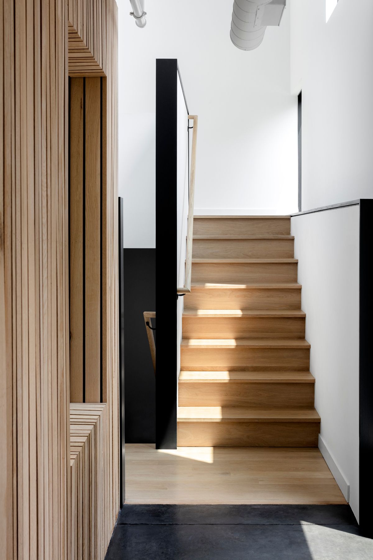 Modern staircase with wooden steps in a bright minimalist interior, sunlight casting shadows on the stairs