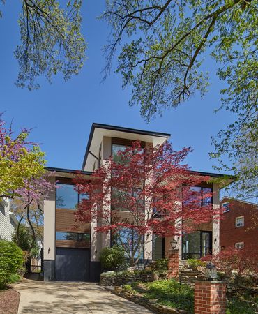 Modern two-story house with brick accents, red-leaf trees, and a blue sky viewed from the front yard