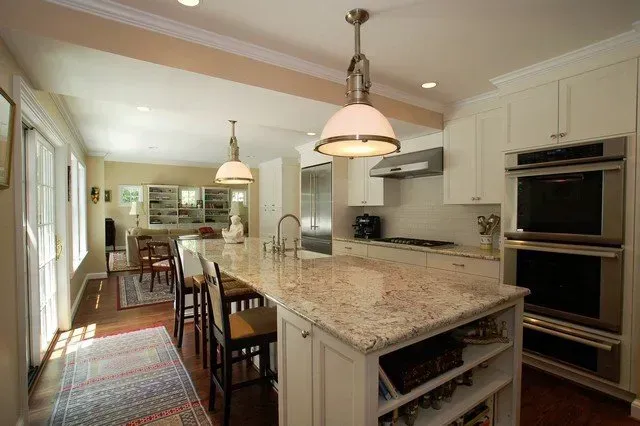 Bright kitchen with marble island, pendant lights, bar stools, and built-in double ovens