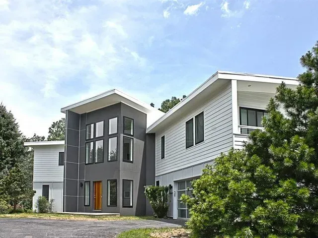 Modern apartment building with gray and white siding, large windows, and trees in front