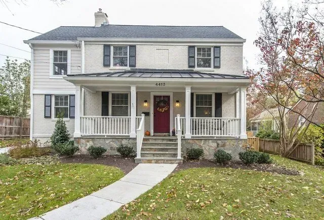 Two-story white house with front porch, gray roof, red door, and a walkway through a leaf-covered lawn.