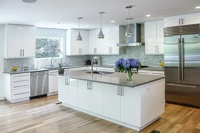 Modern white kitchen with island, stainless steel appliances, pendant lights, and wood floors