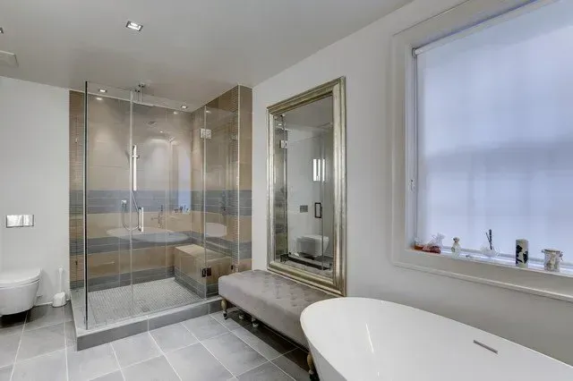 Modern bathroom with glass shower, freestanding tub, large mirror, and neutral gray tile.