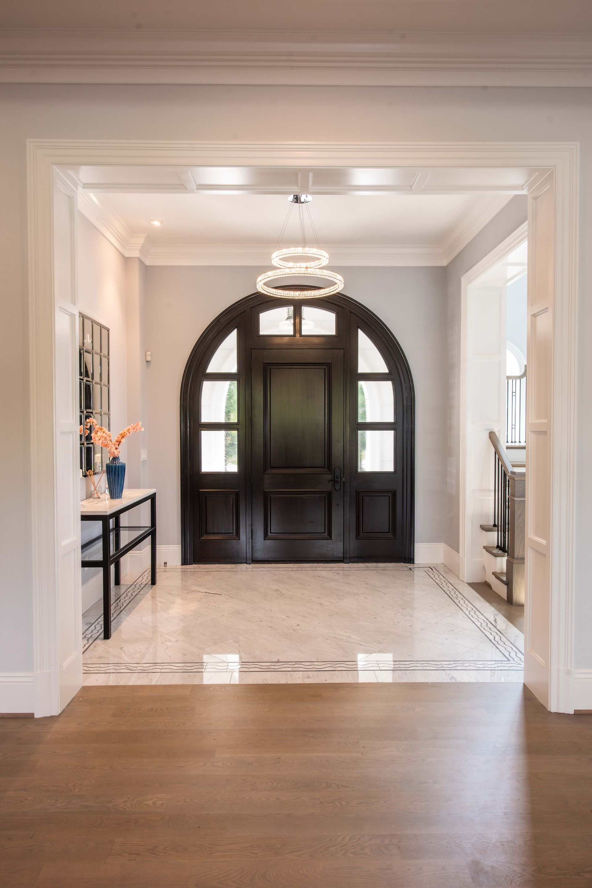 Bright foyer with dark wood arched front door, chandelier, and tiled entryway viewed from a hallway.