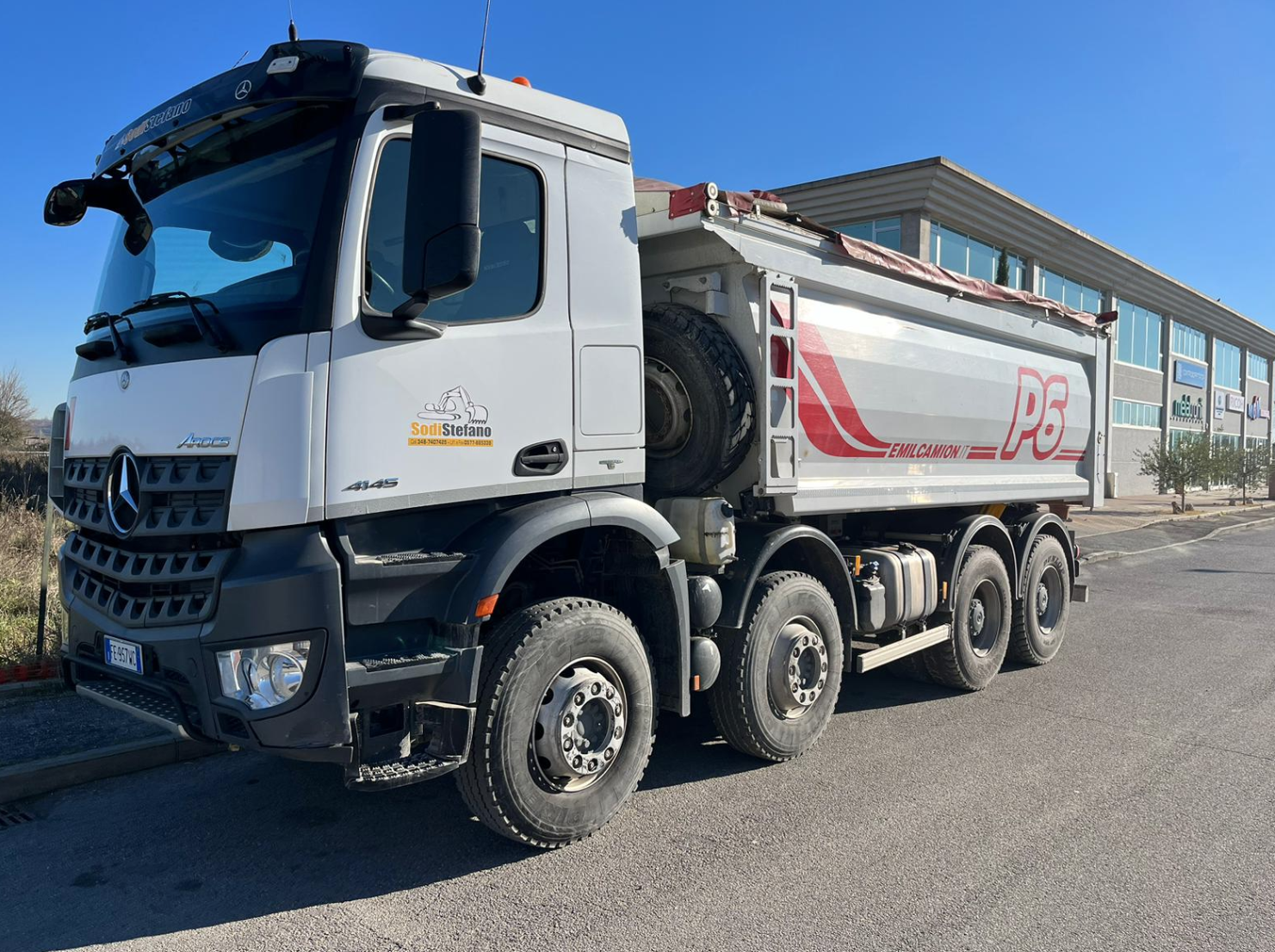 Un camion con cassone ribaltabile è parcheggiato sul ciglio della strada di fronte a un edificio.
