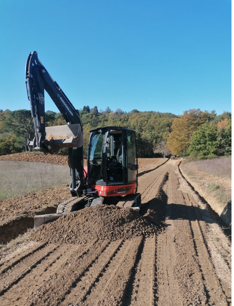 Un escavatore sta scavando una buca nel terreno di una strada sterrata.