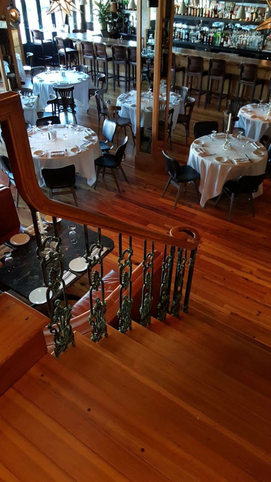 Interior of a restaurant with set white-clothed tables, wooden floors, and a staircase railing in the foreground