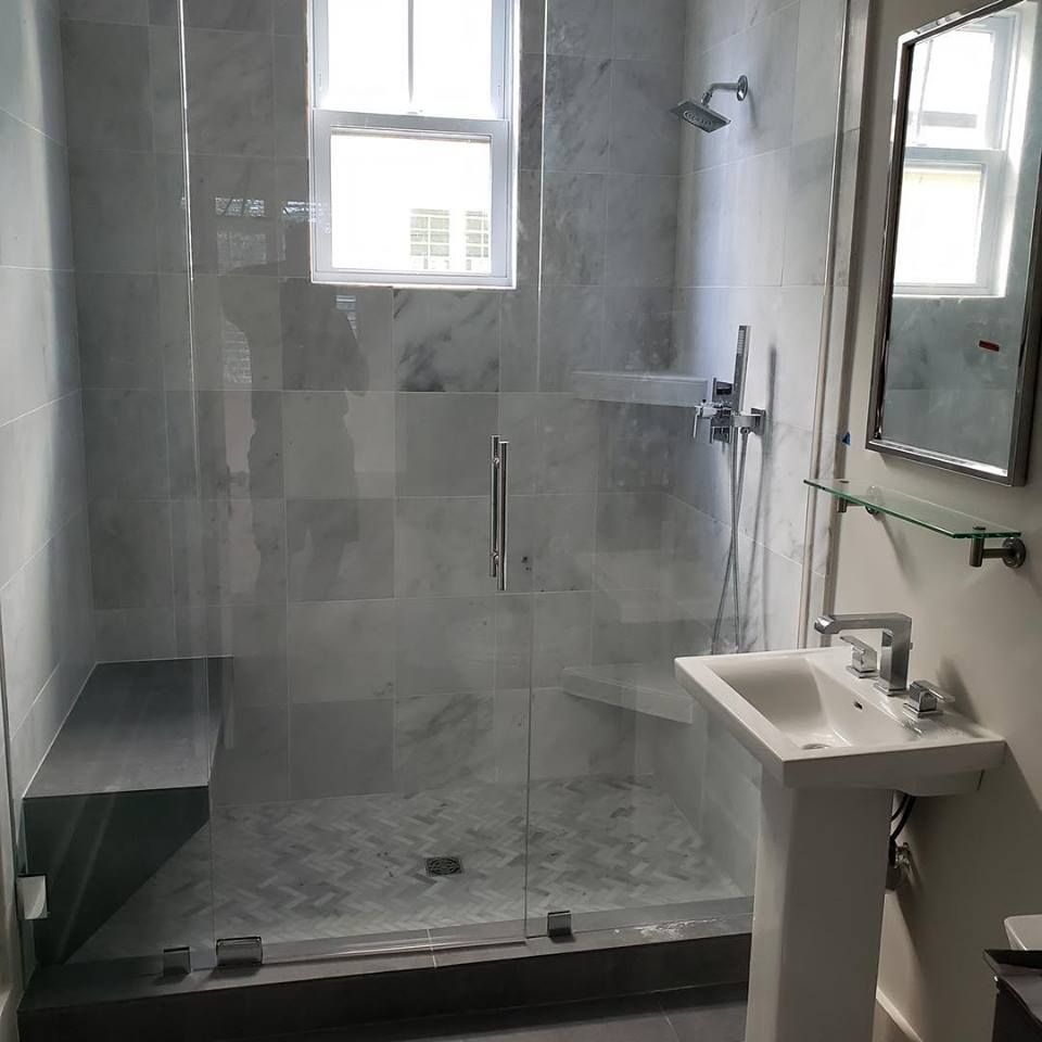 Modern bathroom with glass shower, gray tile, window, sink, and mirror