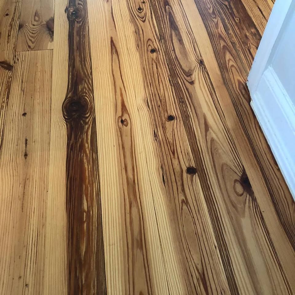 Close-up of a honey-colored wooden floor with visible knots and grain, beside a white wall or door trim.