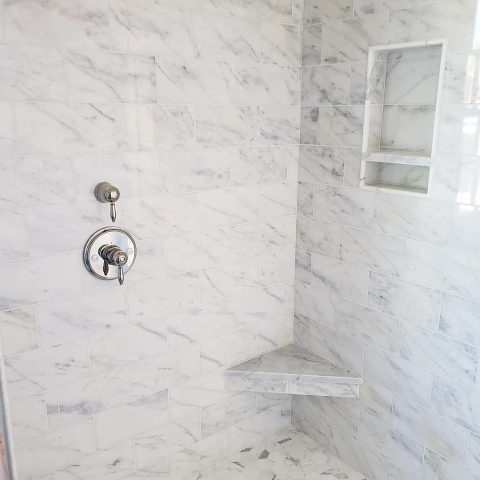 Tiled shower with chrome fixtures, corner shelf, and recessed niche in a bright bathroom.