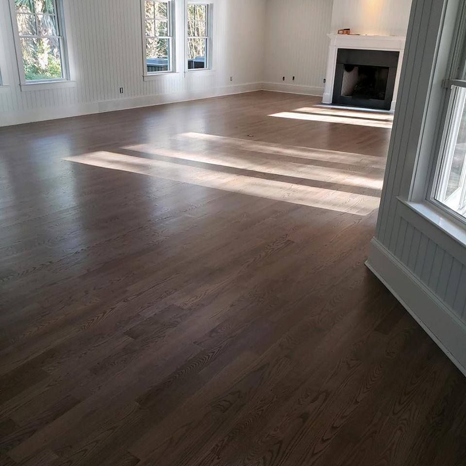 Empty room with hardwood floors, white walls, large windows, and a fireplace with sunlight streaming in