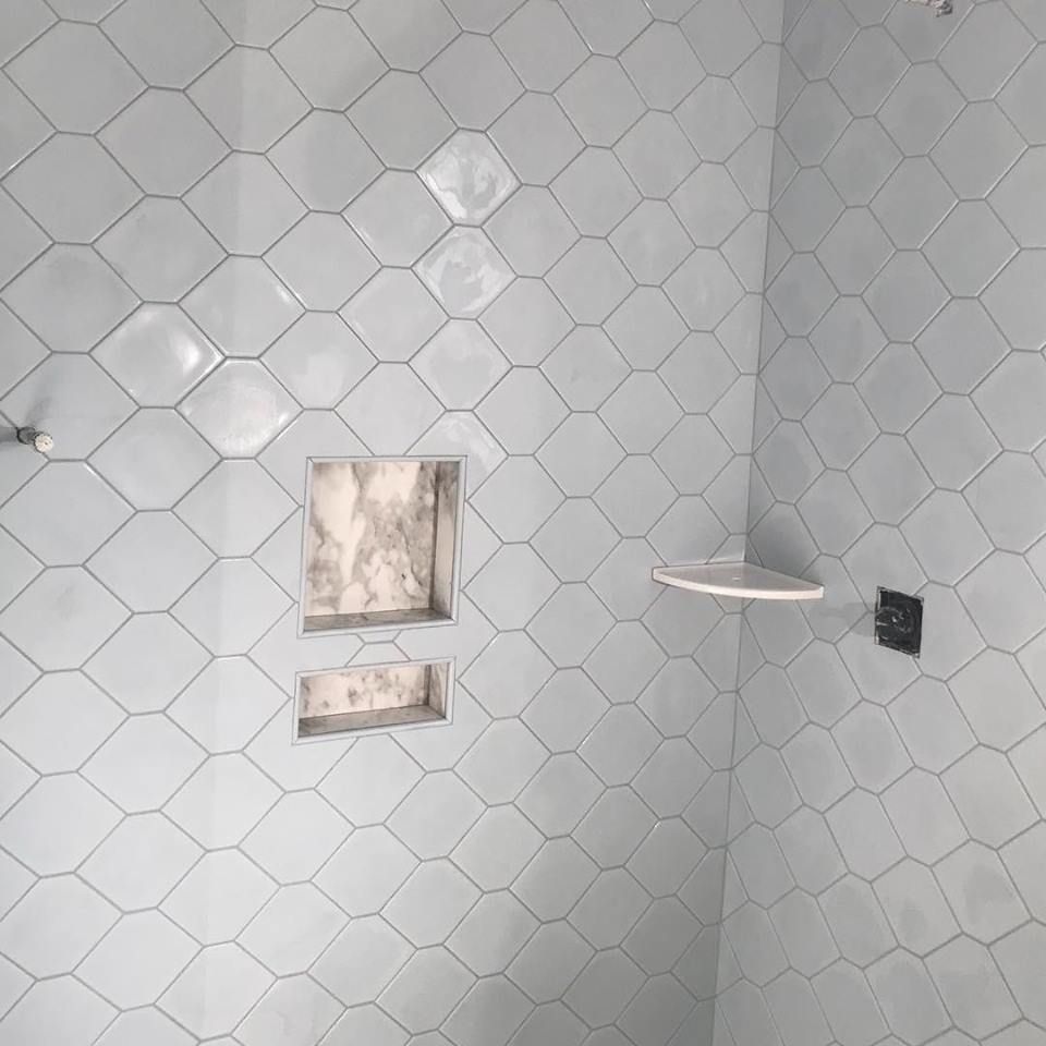 Small tiled bathroom corner with shower head, two recessed wall niches, and a wall outlet.