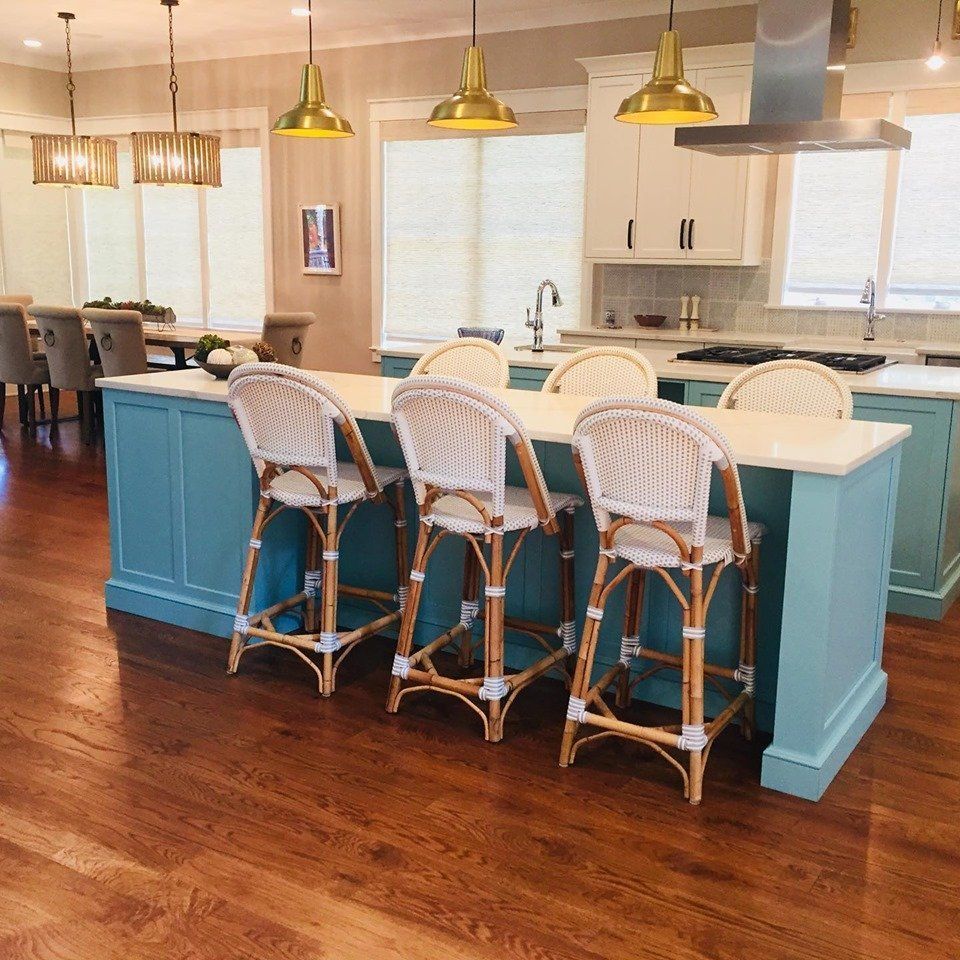 Bright kitchen with teal island, wicker barstools, white cabinets, and gold pendant lights on wood floors