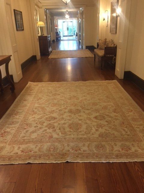 Elegant hallway with a large patterned rug on hardwood floors, leading to a bright doorway.