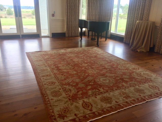 Spacious living room with a large red patterned rug, wooden floor, and floor-to-ceiling windows.