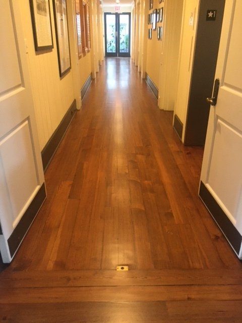 Narrow hallway with polished wooden floor, cream walls, and doors lining both sides.
