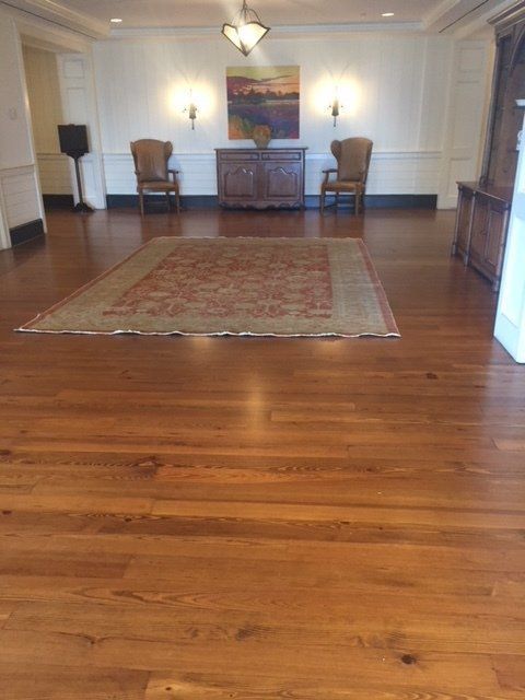 Empty hardwood-floored room with a red rug, chairs, and a sideboard against a white wall