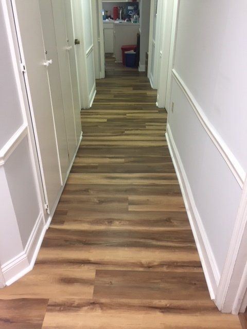 Narrow hallway with white walls and wood-patterned flooring, doors on both sides.