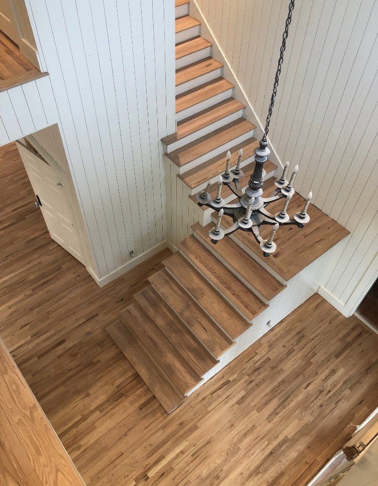 Top-down view of a wooden staircase and landing with a modern chandelier hanging over the foyer