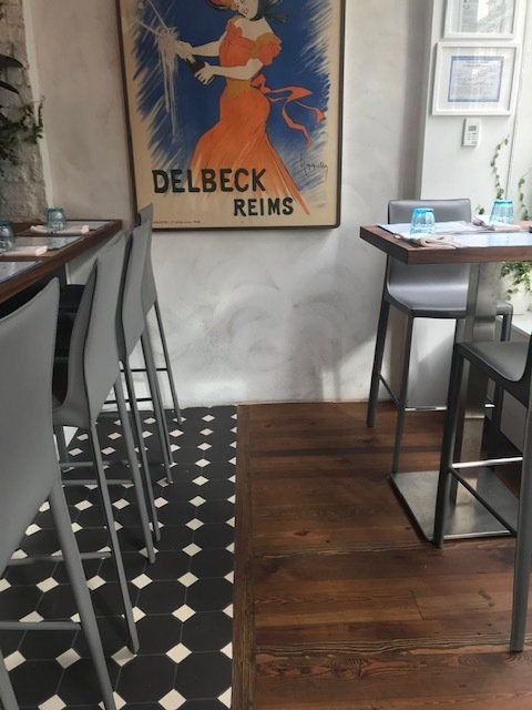 Cozy cafe interior with black-and-white tile floor, wooden tables, and a vintage Delbeck Reims poster.