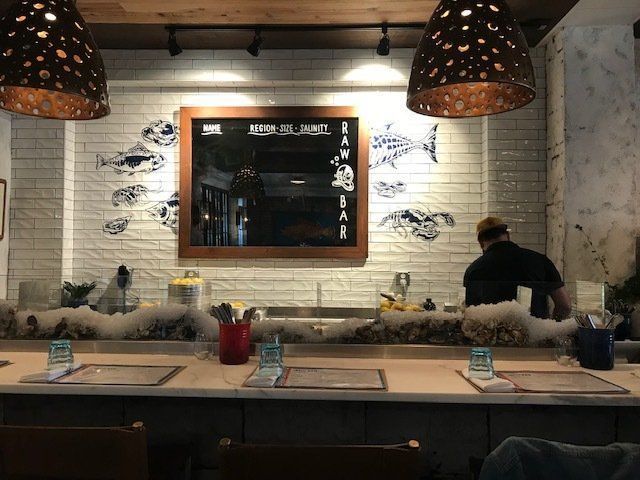 Cozy restaurant counter with hanging lamps, chalkboard menu, and a staff member behind the bar