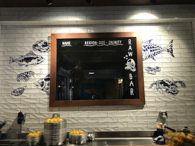 Rustic bar counter with lemons, framed mirror, and fish wall art on a white brick wall.