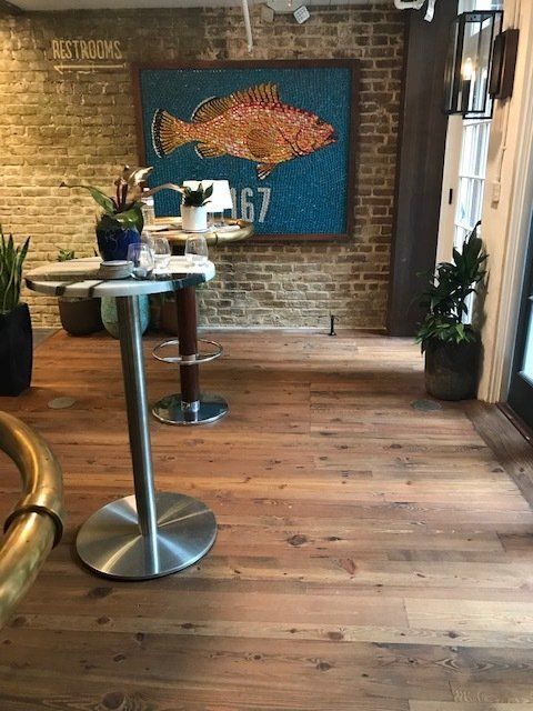 Modern restaurant interior with brick walls, wood floor, high tables, stools, and wall art of a fish-shaped map