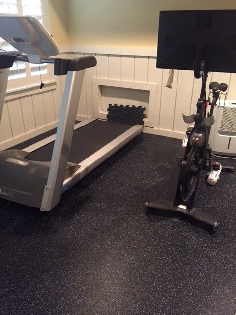 Treadmill and stationary bike in a small home gym with black flooring and white paneled walls