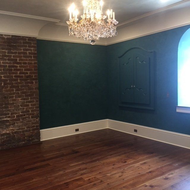 Empty room with dark green walls, hardwood floor, brick accent wall, chandelier, and window light.