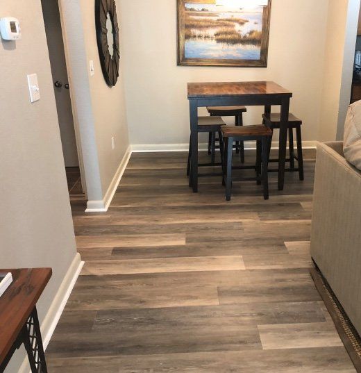 Small dining table with stools in a living room hallway, wood-look floor and beige walls.