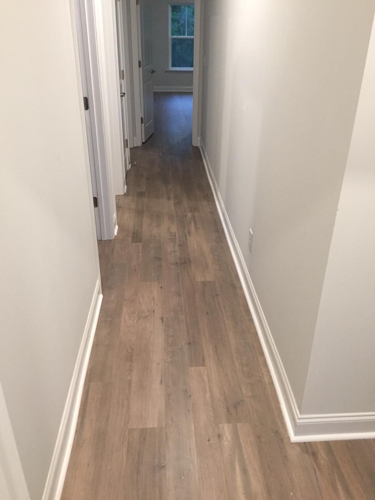 Narrow hallway with white walls and wood-look flooring leading to a windowed room.