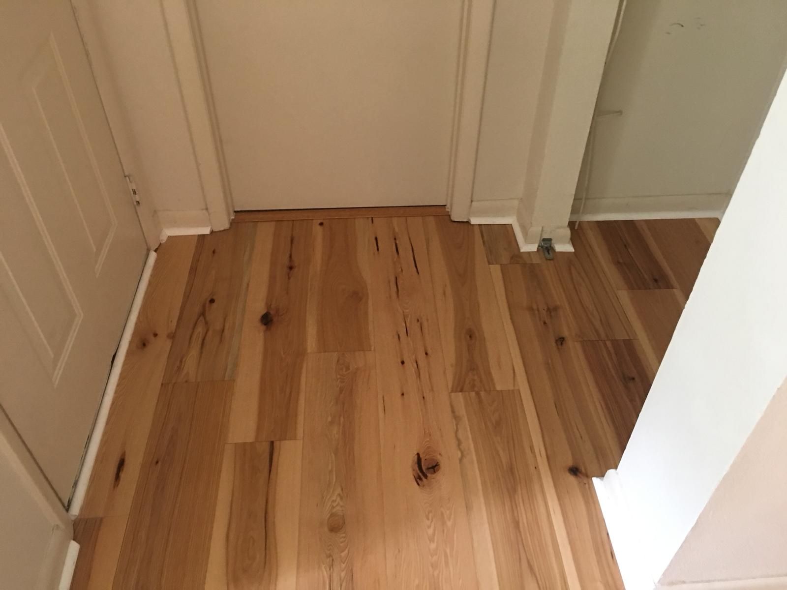 Wooden hallway floor with white walls and doorways, viewed from a corner.