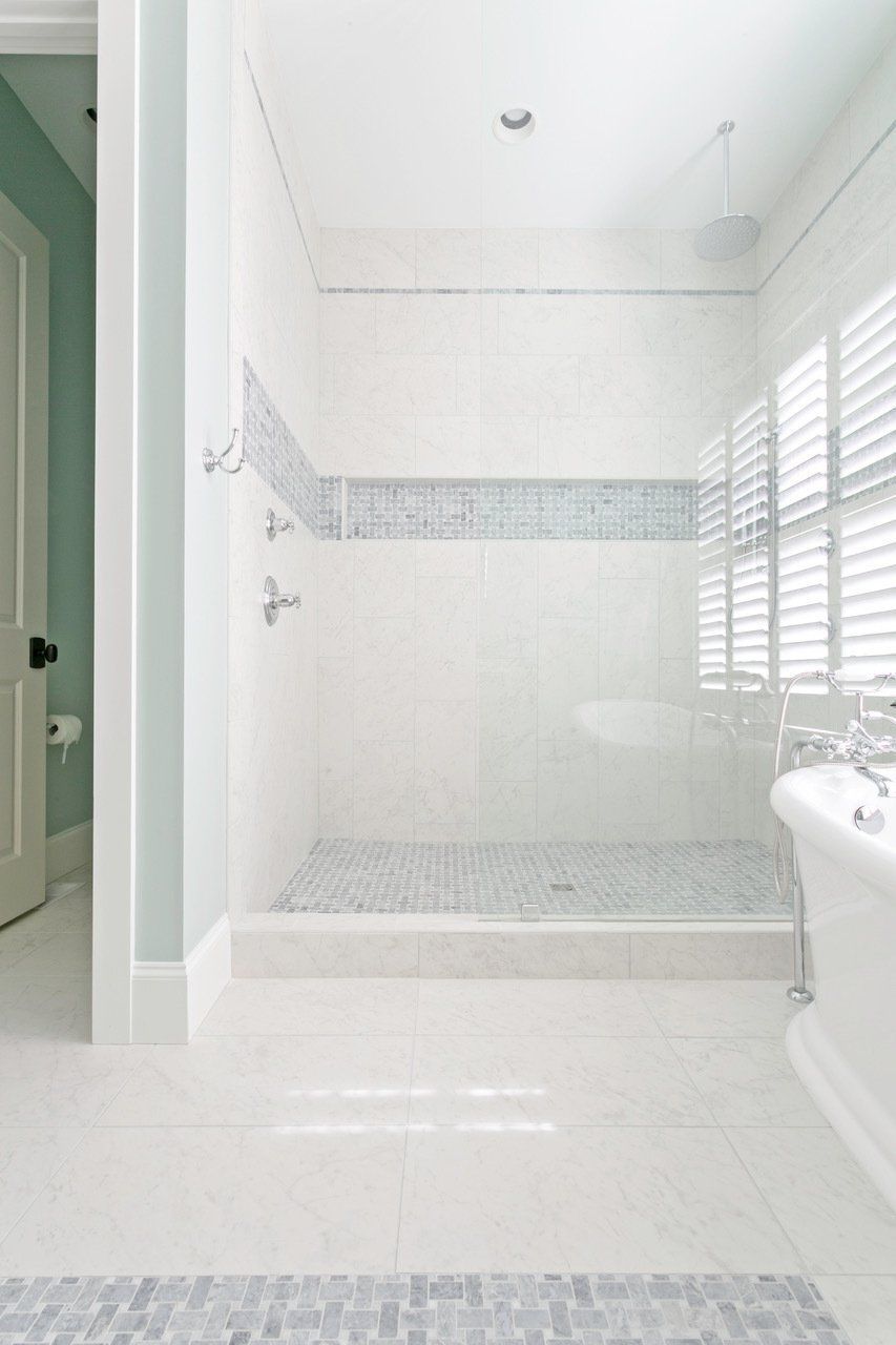 Bright bathroom with glass shower enclosure, beige tile walls, and hexagon floor tiles